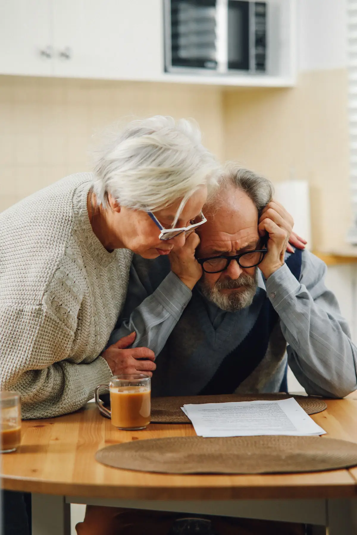 Two people sitting at a kitchen table looking at a stack of documents.